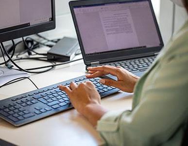 在键盘上打字的人看着笔记本电脑和显示器