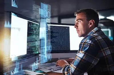 person sitting in front of multiple computer monitors looking at computer code